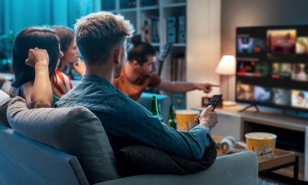 Hands holding a film ticket and remote beside a printed ratings chart and a short review excerpt on a table