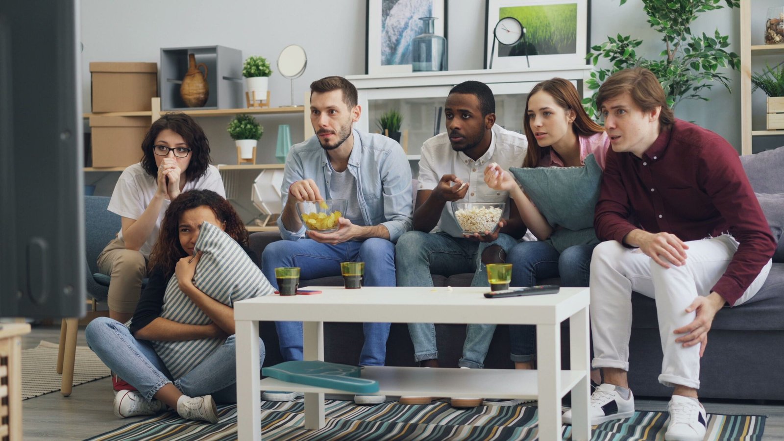Group of people discussing a TV show on devices, one person signaling to pause the conversation