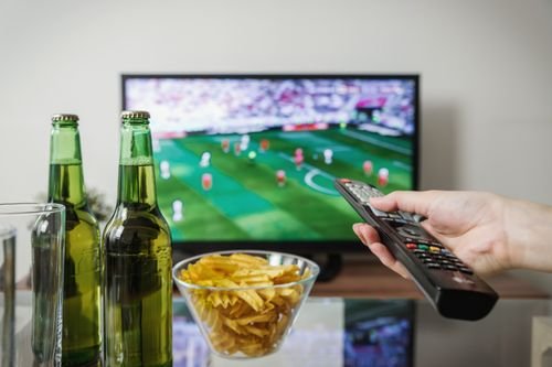 Traveler in a hotel room using hotel Wi‑Fi to stream a live sports match on a laptop with a mobile device showing the hotel internet login page.